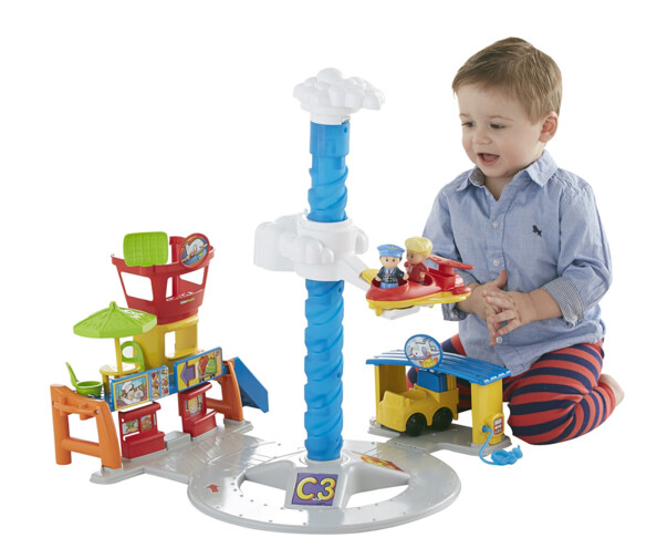 Enfant en bas âge à genou devant l'aéroport Little People Fisher Price dont l'avion contenant le pilote et le passager tourne en rond autour d'un axe en spirale bleu sur une plateforme similaire à une piste de décollage et d'atterrissage