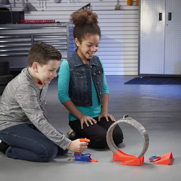 Petit garçon et petite fille assis au sol dans un garage lançant à toute vitesse des petites voitures dans un looping et sur une rampe pour faire des cascades automobiles miniatures