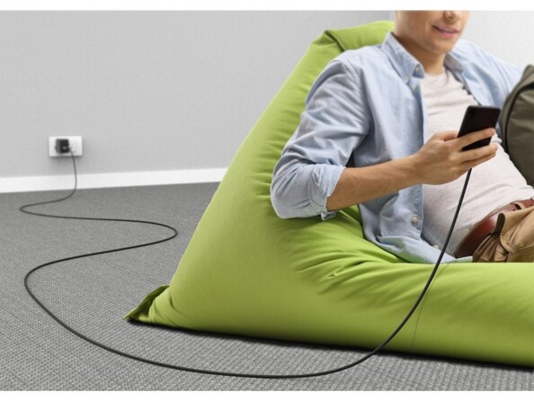 Mise en situation du branchement du câble USB à une prise de courant et à un smartphone regardé par un jeune homme affalé dans un pouf