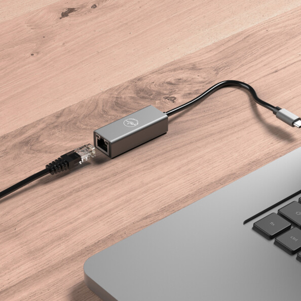 Mise en situation du hub réseau USB externe en cours de branchement au port USB-C d'un ordinateur portable et à un câble réseau RJ45 sur une surface en bois clair