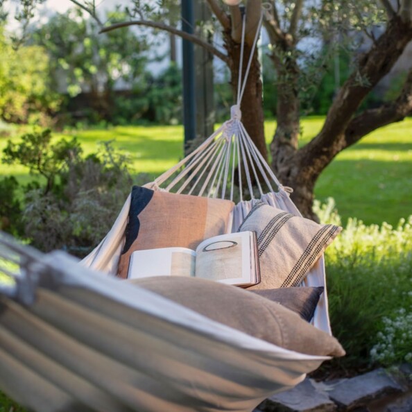 Hamac fixé à deux arbres en pleine nature comme couchage d'appoint avec oreillers et livres posés dedans
