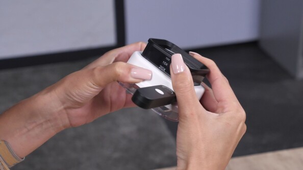 Deux mains d'une personne règlant le grossissement de la loupe à main sur le côté du boîtier blanc et noir, à côté de la poignée rotative