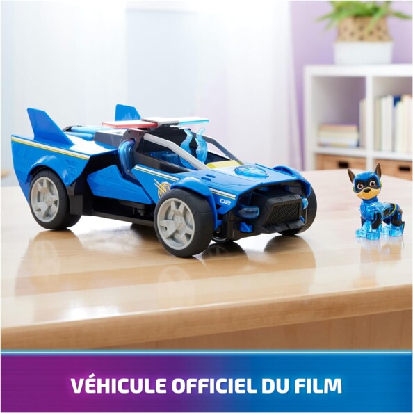Véhicule officiel du film La Pat' Patrouille : La Super Patrouille Le Film et sa figurine Chase posés sur une table en bois laqué d'un salon