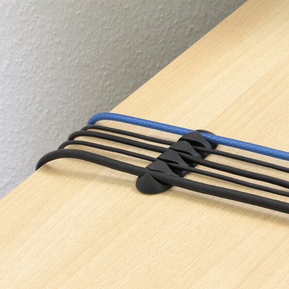 Passe-câbles à 4 fentes installé sur un bureau aspect bois clair et organisant quatre câbles en ordre