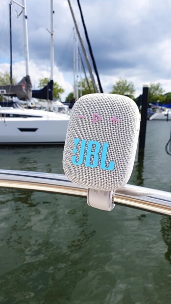 Enceinte suspendue par sa sangle blanche en extérieur avec son logo cyan lumineux