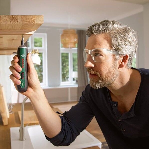 Homme en lunettes vissant avec la visseuse Bosch PushDrive au-dessus d’un plan de travail