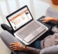 Vue plongeante sur un homme tatoué assis dans un fauteuil avec un PC portable allumé sur les genoux posé sur le support sans fil pour PC Logitech