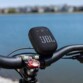 Enceinte JBL fixée au guidon d'un vélo arrêté devant un plan d'eau par le biais du support pour guidon fourni en accessoire