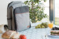 Sac de pique-nique gris fermé posé sur une table en intérieur avec différents accessoires et en-cas sortis du sac pour déjeuner