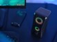 Vue du dessus d'une enceinte stéréo colonne avec rétroéclairage RVB, touche tactile et bouton de réglage du volume à côté d'un PC gamer et d'un smartphone affichant l'écran d'accueil