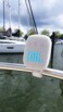 Enceinte suspendue par sa sangle blanche en extérieur avec son logo cyan lumineux